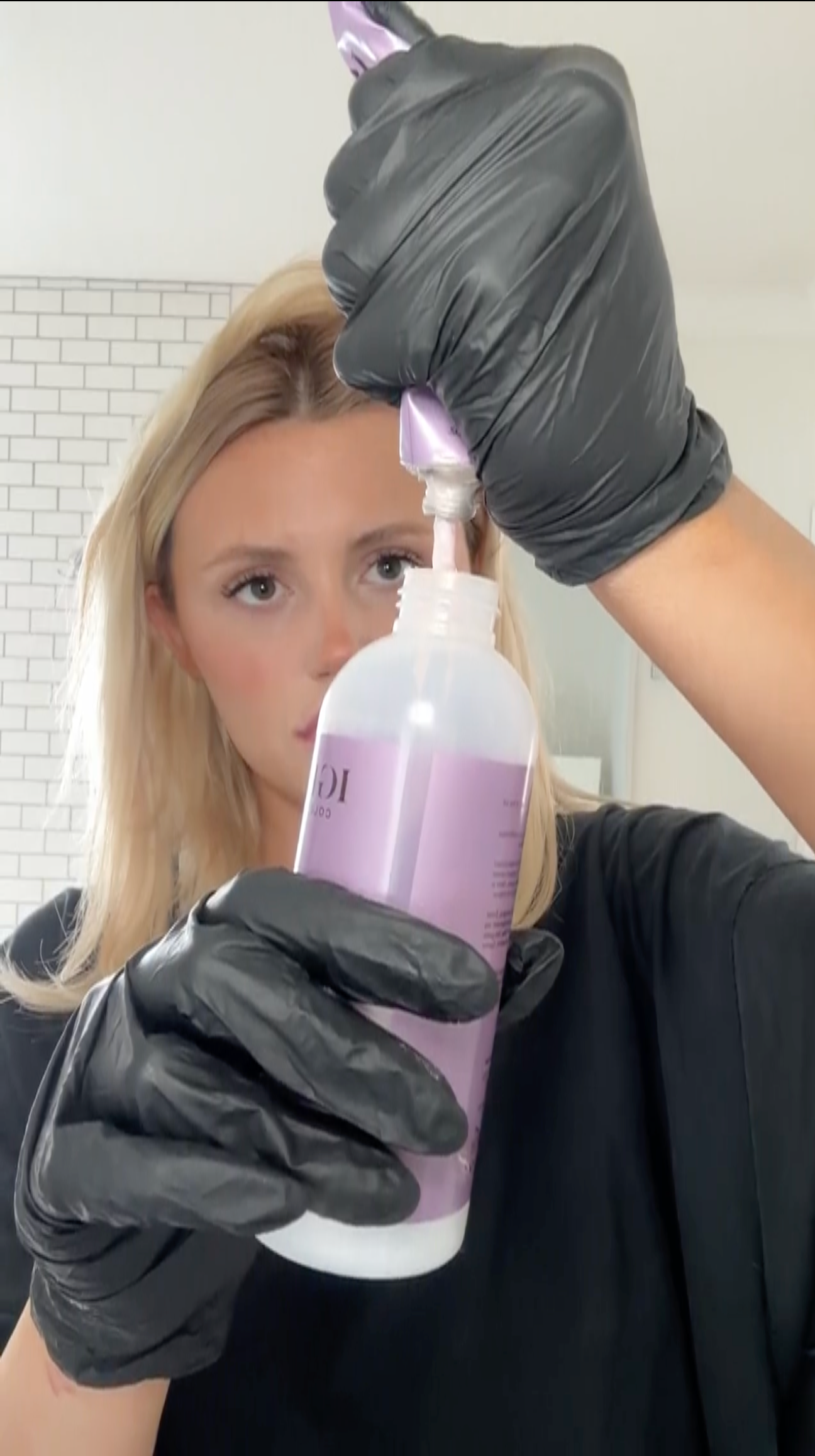 a woman wearing black gloves and holding a bottle with pink liquid