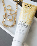 a white and gold bottle of hair balm and gold jewelry